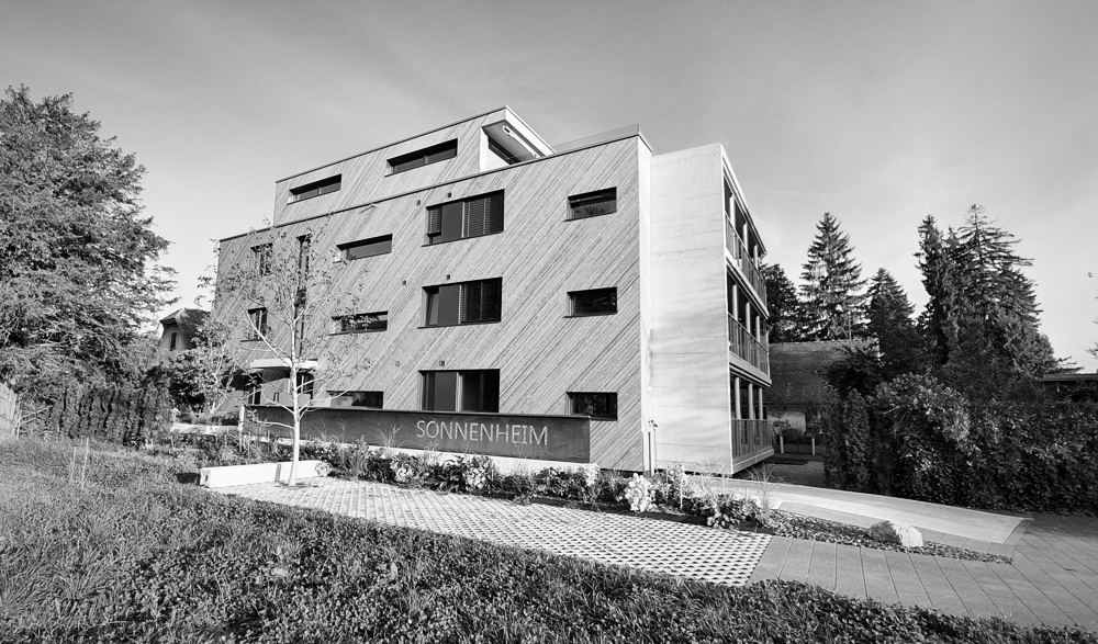 Mehrfamilienhaus Sonnenheim mit diagonaler Holzschalung und Cortenstahl-Schriftzug